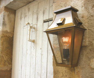 klassische Außenleuchten Vieille France, Roger Pradier klassische Außenleuchte an einer Hauswand aus Naturstein, neben Tür. Klarglas, Wandlampe ist aus Messing.